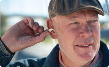 Ældre mand, der bruger høreapparat og har behov for Otinova ørespray.